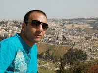 a man in sunglasses standing on a hill overlooking a city